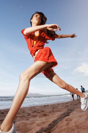 Téléchargez les photos : Dance Freedom by the Sea : un mannequin joyeux et insouciant qui court sur la plage au coucher du soleil sous le ciel rouge et bronzé - en image libre de droit