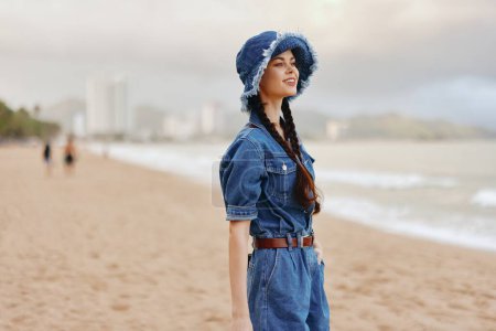 Foto de Vacaciones relajadas en la playa: Atractiva mujer caucásica disfrutando del sol y el mar de verano con elegante vestido y sombrero - Imagen libre de derechos