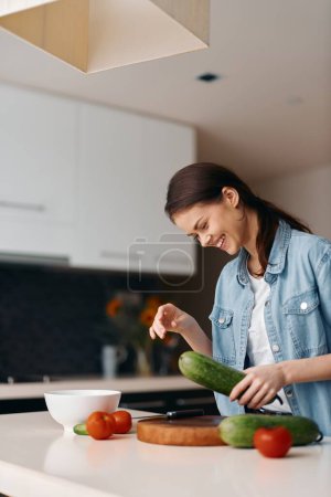 Téléchargez les photos : Cuisine maison saine : Une jeune cuisinière prépare une salade végétarienne fraîche dans un intérieur magnifiquement décoré - en image libre de droit