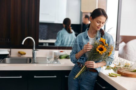 Téléchargez les photos : Jeune femme dans la cuisine cueillant un bouquet de fleurs de tournesols, mode de vie des femmes Deni, fleuriste au travail. Photo de haute qualité - en image libre de droit