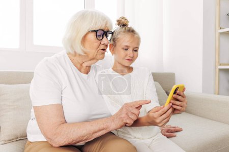 Photo for Selfie photography child family t-shirt sofa two white granddaughter phone call indoors smiling togetherness copy video bonding space people happiness grandmother education hugging - Royalty Free Image
