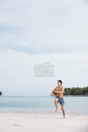Foto de Hombre asiático activo disfrutando de la carrera de playa al atardecer: atleta muscular abrazando la aptitud y el bienestar al aire libre - Imagen libre de derechos