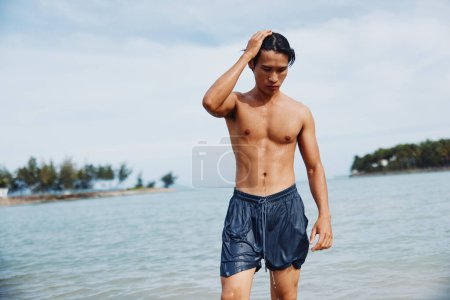 Téléchargez les photos : Tropical Splash : Un Asiatique Souriant Embrasser la Liberté dans l'Océan Bleu, Profiter d'une baignade estivale active - en image libre de droit
