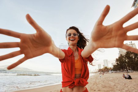 Téléchargez les photos : Femme souriante à la plage, profiter de la liberté de la mer sous un coucher de soleil coloré - en image libre de droit