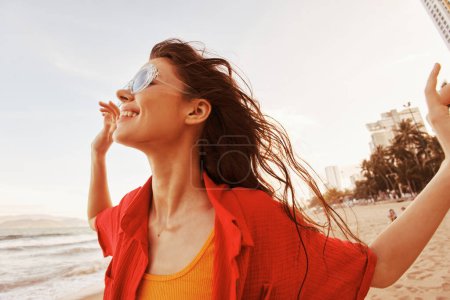 Foto de Mujer sonriente con gafas de sol, abrazando la libertad: retrato vibrante de belleza alegre al atardecer en la playa - Imagen libre de derechos