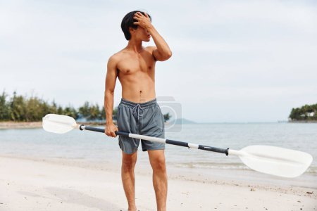Téléchargez les photos : Homme asiatique actif profitant de l'aventure d'embarquement SUP au coucher du soleil sur une plage - en image libre de droit