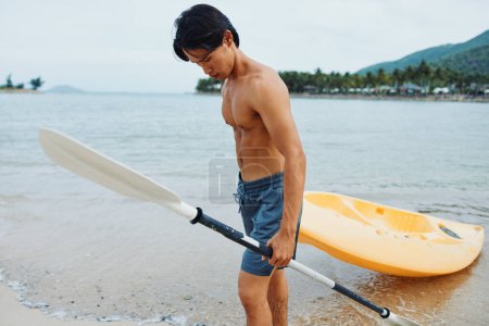 Téléchargez les photos : Happy Asian Man Canoë-kayak dans une aventure de kayak tropical sur une plage - en image libre de droit