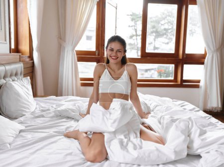 Photo for Brunette young woman on bed wrapped in white blanket at home in the morning. Sensual young woman in lingerie with sexy body in modern apartment after waking up. weekend, vacation. High quality photo - Royalty Free Image