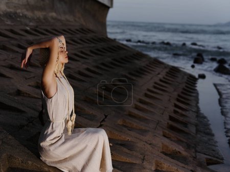Téléchargez les photos : Voyageuse solitaire assise seule sur la plage de sable, regardant les vagues envoûtantes sous un ciel romantique au coucher du soleil. - en image libre de droit