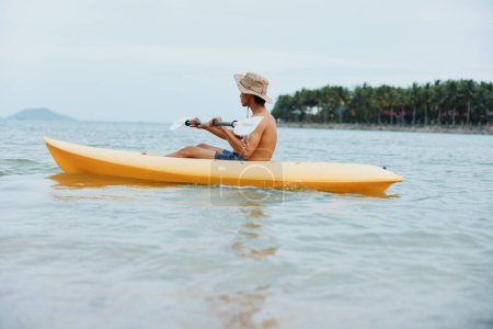 Téléchargez les photos : Fun in the Sun : Un Asiatique Actif Profitant du kayak sur une plage tropicale - en image libre de droit