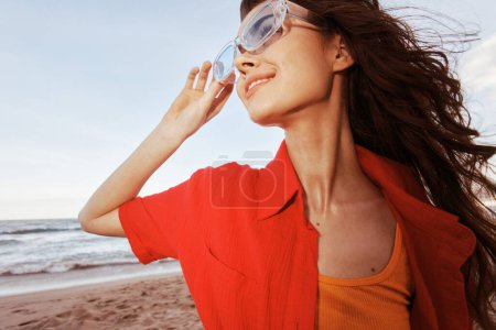 Téléchargez les photos : Sheer Joy : Femme souriante embrassant la liberté dans les lunettes de soleil colorées, bonheur au coucher du soleil sur Sandy Beach - en image libre de droit