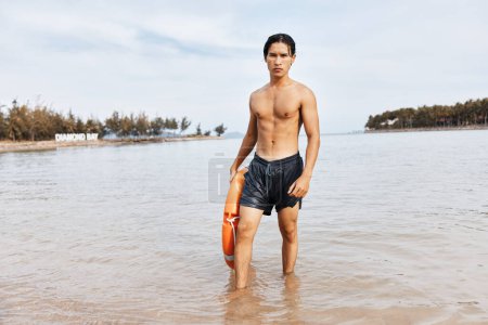 Téléchargez les photos : Sauveteur secourant un nageur sur la plage avec une bouée de sauvetage : un symbole de sécurité, de protection et de joie. - en image libre de droit