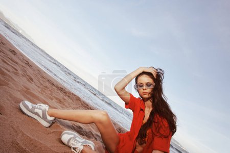 Téléchargez les photos : Mode drôle : Femme souriante assise sur une plage étrange. - en image libre de droit