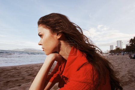 Téléchargez les photos : Portrait insouciant d'une belle femme assise sur la plage, jouissant de la liberté et de la sérénité de l'océan au coucher du soleil - en image libre de droit