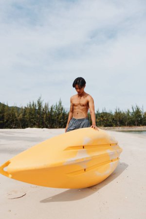 Téléchargez les photos : Kayak Fun : L'homme asiatique profite de vacances actives à la plage avec pagaie et canot dans le paradis tropical - en image libre de droit