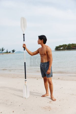 Téléchargez les photos : Aventure sur la plage : Homme asiatique actif Paddleboard au coucher du soleil, profiter des sports nautiques et se détendre dans la nature - en image libre de droit