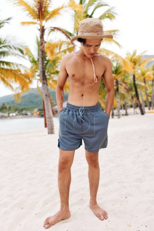 Foto de Vacaciones en la playa: Hombre asiático musculoso con una sonrisa feliz, disfrutando del océano y las palmeras en una isla tropical - Imagen libre de derechos