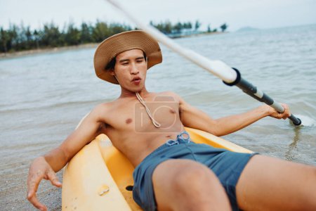 Photo for Happy Asian Man Enjoying Kayaking Adventure on Tropical Beach - Royalty Free Image