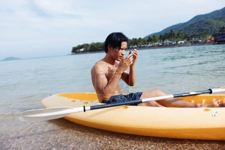 Téléchargez les photos : Serene Summer Fun : Un homme asiatique heureux faisant du kayak sur une plage tropicale - en image libre de droit