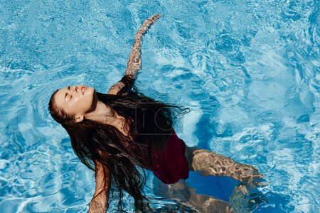 Téléchargez les photos : Femme heureuse nageant dans la piscine en maillot de bain rouge avec les cheveux longs lâches, protection de la peau avec écran solaire, concept de détente en vacances. Photo de haute qualité - en image libre de droit