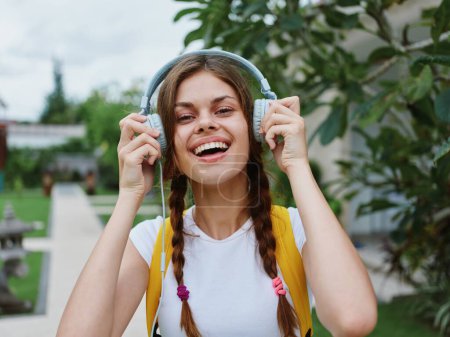 Foto de Mujer joven mira a la cámara de la felicidad viaja de vacaciones con una mochila y auriculares escuchando música con una sonrisa caminando fuera. Foto de alta calidad - Imagen libre de derechos