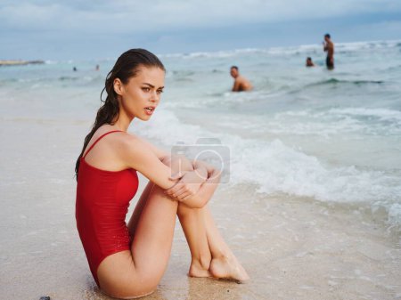 Téléchargez les photos : Une femme triste est assise sur le sable de la plage, les bras autour des jambes, regardant le soleil se coucher sur une île tropicale. Photo de haute qualité - en image libre de droit
