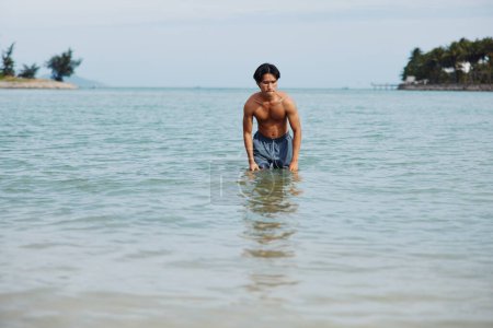 Téléchargez les photos : Happy Asian Man Profiter d'une baignade relaxante dans l'océan bleu tropical - en image libre de droit