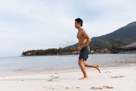 Téléchargez les photos : L'homme asiatique athlétique embrassant la liberté et le bien-être tout en courant sur la plage au coucher du soleil - en image libre de droit
