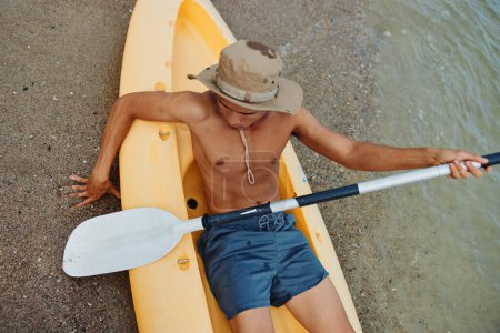 Téléchargez les photos : Sérénité embrassée par le soleil : Un homme asiatique profite d'une aventure de kayak sur une plage tropicale - en image libre de droit
