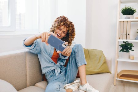 Téléchargez les photos : Happy Woman tenant téléphone portable, se détendre sur le canapé à la maison - Technologie confortable - en image libre de droit