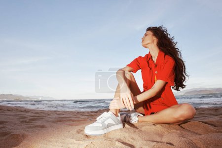 Téléchargez les photos : Femme souriante en tenue tendance, se détendre sur la plage : un portrait du bonheur et de la beauté dans les environs naturels. - en image libre de droit