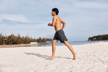 Téléchargez les photos : Musclé asiatique homme profiter de vacances sur belle plage tropicale, sourire avec joie - en image libre de droit