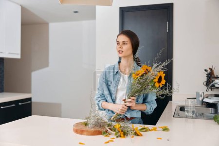 Photo for Pretty Caucasian Woman Standing in Green Kitchen with Flower Bouquet: A Young, Attractive Ladys Happy Summer Lifestyle in a Stylish Floral Interior. - Royalty Free Image