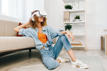 Photo for Smiling woman enjoying virtual reality game at home with futuristic VR goggles on sofa in a modern living room - Royalty Free Image