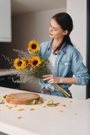 Foto de La hermosa mujer caucásica en la cocina, cocinando una comida vegetariana saludable en una mesa de madera rodeada de un atractivo interior floral. - Imagen libre de derechos
