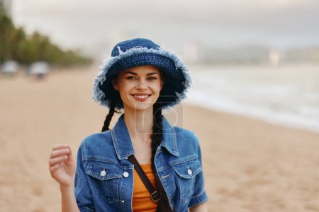 Téléchargez les photos : Joyeux jeune femme Profitant de vacances d'été sur la plage, Belle dame en chapeau et bikini à la mode, Souriant avec l'océan bleu et le ciel ensoleillé comme arrière-plan - en image libre de droit