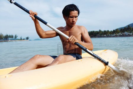 Foto de Feliz hombre asiático disfrutando de Kayak Aventura en Tropical Beach Vacation - Imagen libre de derechos