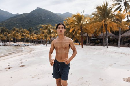 Foto de Hombre asiático activo disfrutando de entrenamiento de fitness al aire libre en la playa al atardecer - Imagen libre de derechos