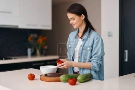 Foto de Comida, salud y felicidad: Una hermosa cocinera joven prepara una ensalada vegetariana fresca en casa. - Imagen libre de derechos