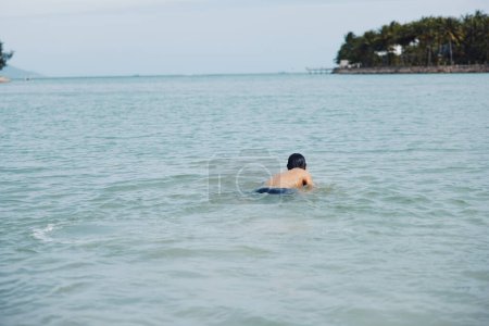 Photo for Smiling Asian man enjoying an active summer vacation: Splash and swim in tropical blue ocean water". - Royalty Free Image