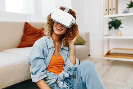 Téléchargez les photos : Femme souriante jouissant d'un jeu de réalité virtuelle à la maison avec des lunettes VR futuristes - en image libre de droit