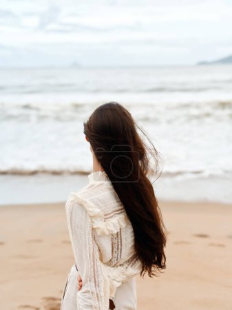 Téléchargez les photos : Femme solitaire marchant seule sur une plage au bord de la mer, regardant la tristesse de l'horizon, embrassant le calme de l'océan - en image libre de droit