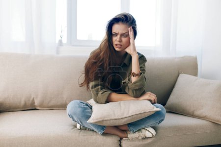 Téléchargez les photos : Femme éprouvant le stress et la dépression, assise sur le canapé se sentant triste et inquiète à la maison - en image libre de droit