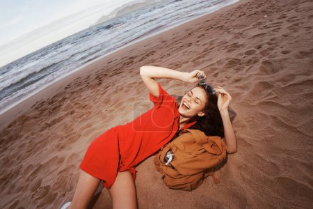 Téléchargez les photos : Joyful Backpacker : Femme voyageuse, ivre de bonheur, se détendre sur la plage de sable fin au bord de la mer - en image libre de droit