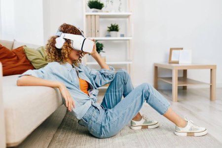Téléchargez les photos : Plaisir de réalité virtuelle : Une femme souriante jouissant d'un jeu VR futuriste sur le canapé à la maison - en image libre de droit