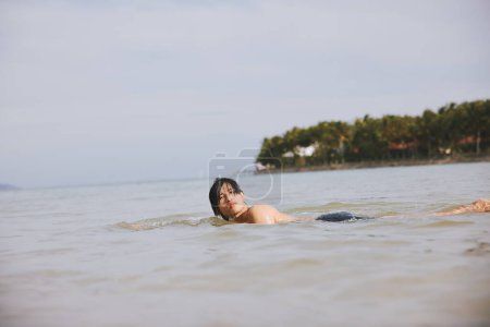 Téléchargez les photos : Joyeux asiatique homme jouissant de sport nautique actif sur une plage tropicale vacances - en image libre de droit