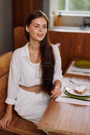 Foto de Mujer sonriente disfrutando de una cena romántica en la mesa de comedor de moda en el elegante comedor con pastel y vino caseros - Imagen libre de derechos