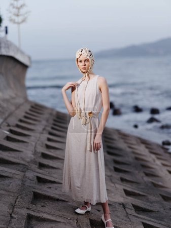 Téléchargez les photos : Beauté et élégance par l'eau bleue : une jeune femme à la mode dans une robe élégante posant à la plage - en image libre de droit