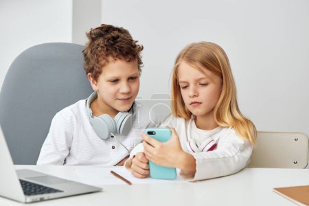 Téléchargez les photos : Heureux enfants caucasiens étudiant en ligne à la maison avec des ordinateurs portables et écouteurs - en image libre de droit