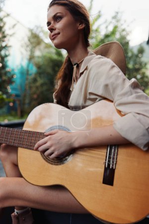 Foto de Una mujer sentada en un banco tocando una guitarra acústica con los pies en el suelo - Imagen libre de derechos